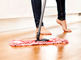 Imagen de una mujer descalza barriendo el piso con un trapeador seco.