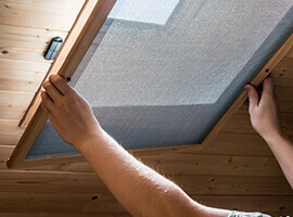 Un hombre instalando un mosquitero en una ventana ubicada en el cielorraso.