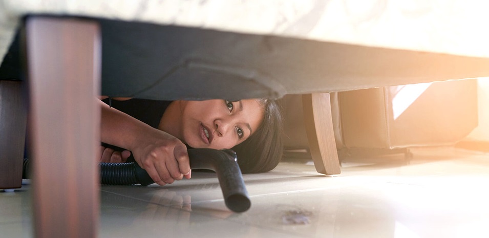 A woman bent down vacuuming underneath her sofa.